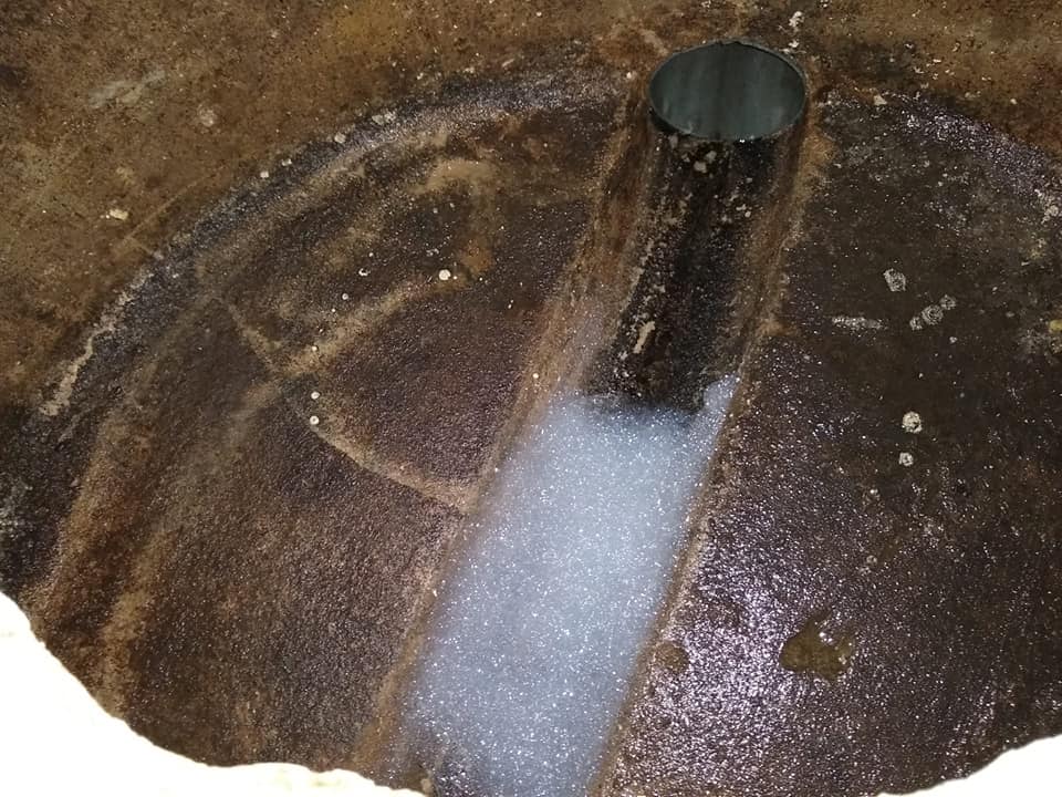 Fossa séptica residencial aberta a mostrar tubo de entrada e lodo decantado no fundo, em fase de inspeção antes de limpeza