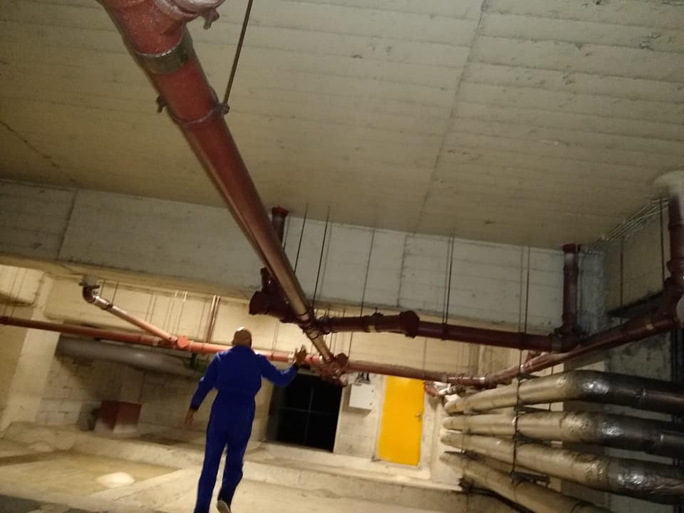 Técnico DesentopeTOP no piso técnico de edifício comercial a inspecionar prumadas de esgoto suspensas no teto