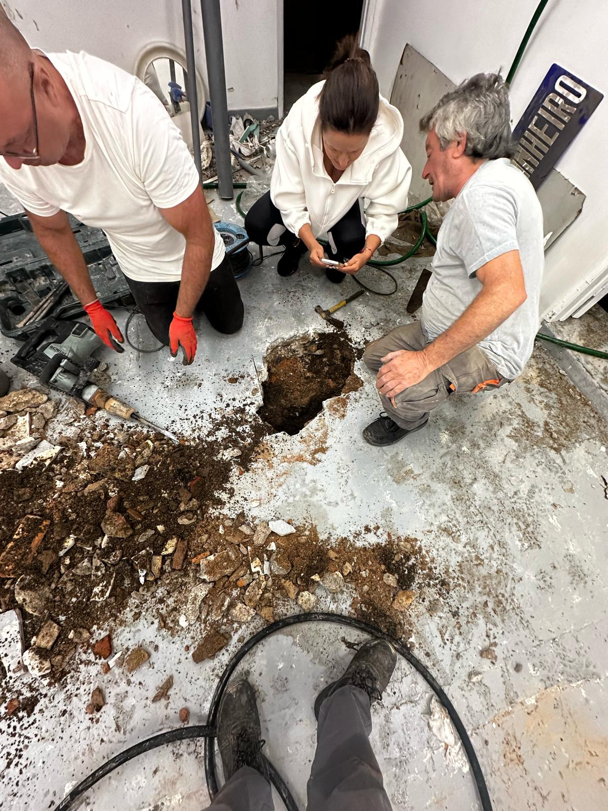 Abertura controlada de pavimento interior com martelo demolidor e equipa a inspecionar a tubagem exposta