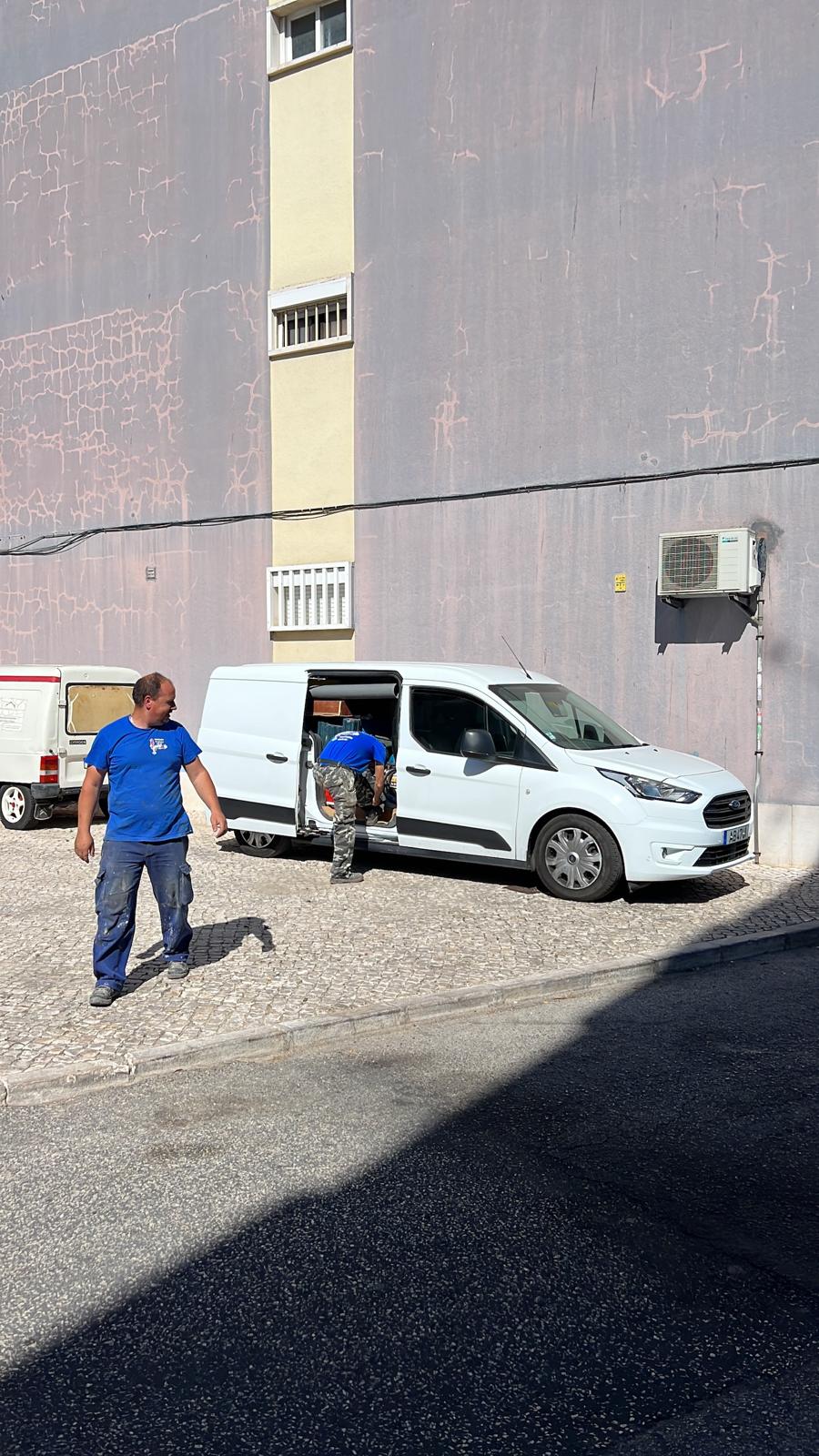 Carrinha de intervenção com porta lateral aberta e equipa a trabalhar junto a um edifício, com acesso pela via pública