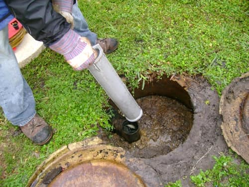 Mangueira de auto-aspirador profissional inserida em tampa de fossa séptica residencial num jardim para limpeza completa